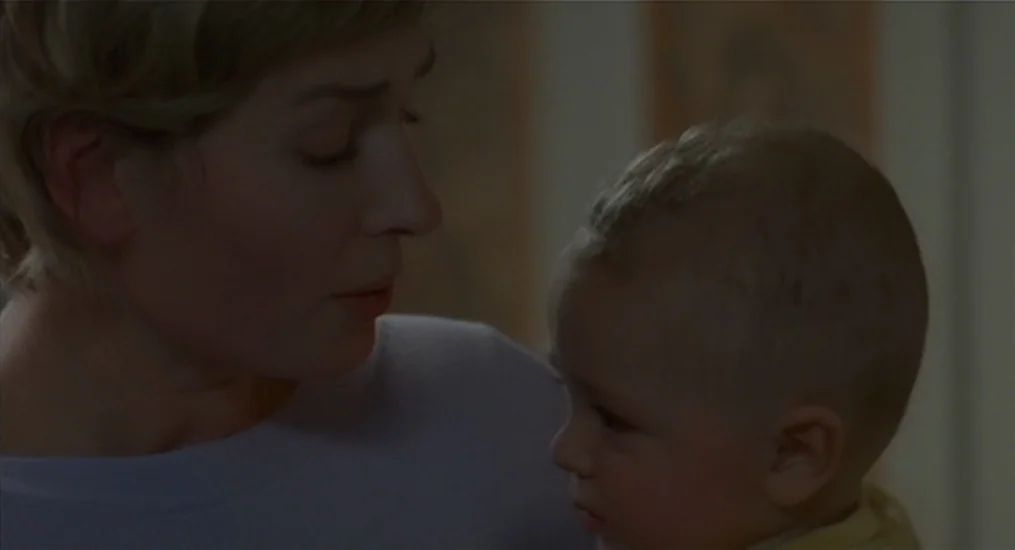 Vendredi Soir (2002) movie still: medium — A woman holding a baby in an indoor space with plain, neutral-colored walls. The woman gazes down at the…