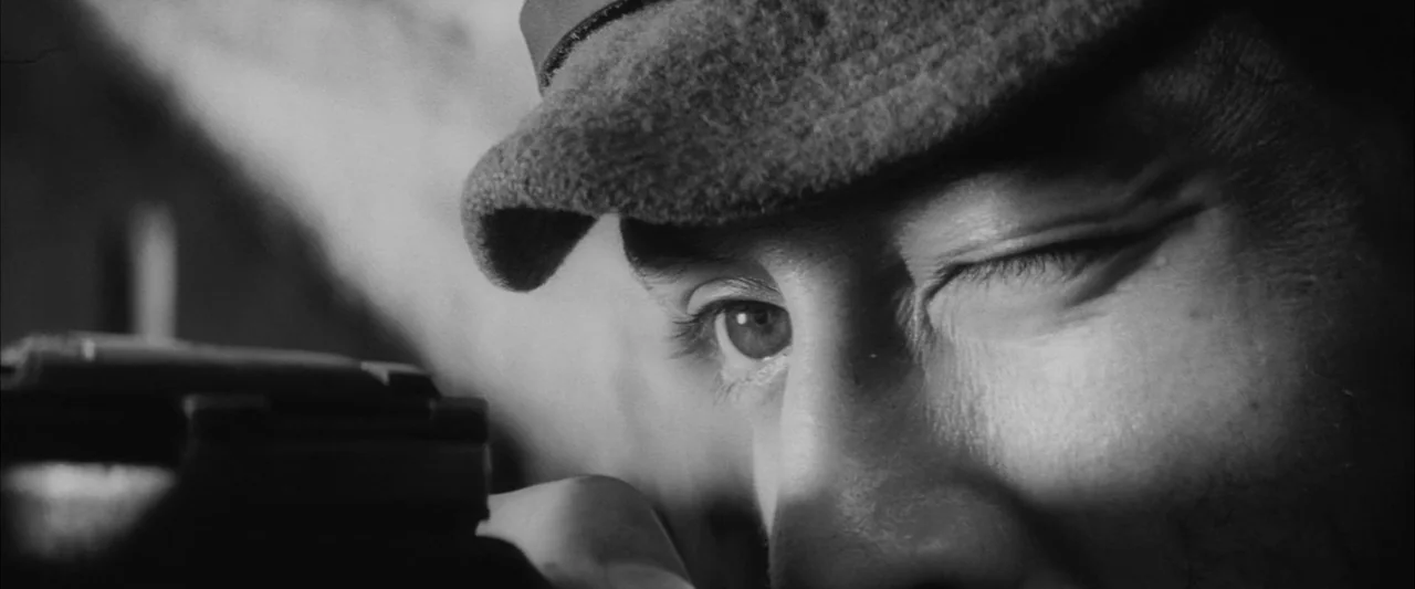 The Human Condition III: A Soldier’s Prayer (1961) movie still: closeup — A close view of a soldier in a military cap aiming a weapon. The…