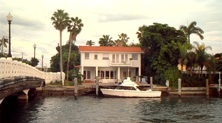 Out Of Sight (1998) movie still: establishing — A two-story white waterfront house stands next to a wooden bridge over a canal. A small white boat…