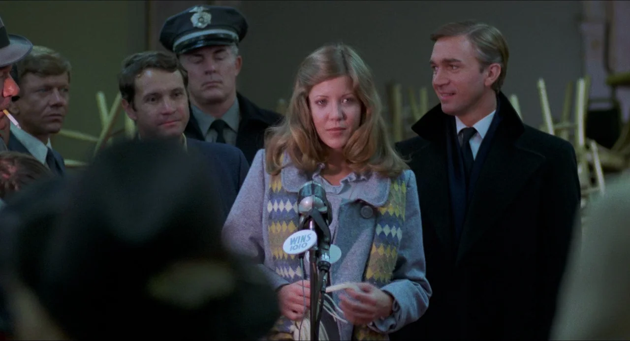 I Wanna Hold Your Hand (1978) movie still: medium — A group of people stands before microphones in an interior room with muted walls. A woman in a…