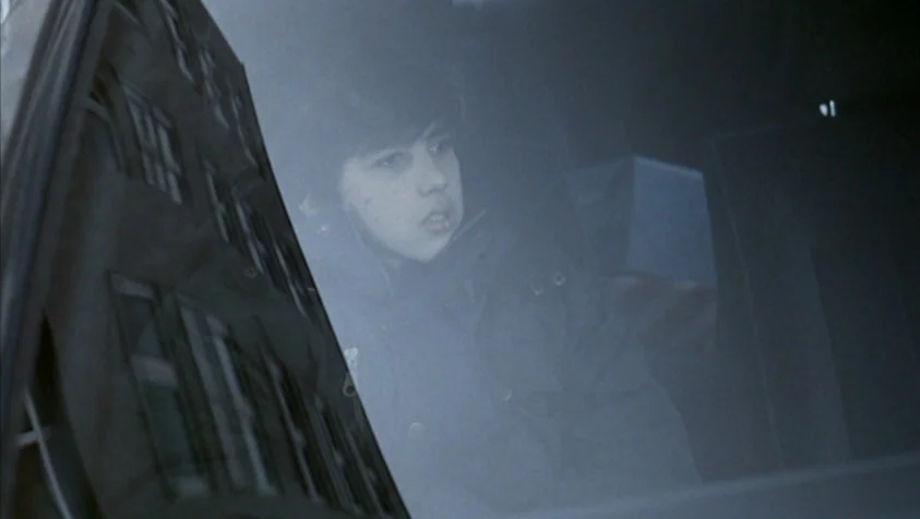 71 Fragments of a Chronology of Chance (1994) movie still: closeup — A person sits inside a car looking through the side window. Reflections of city…