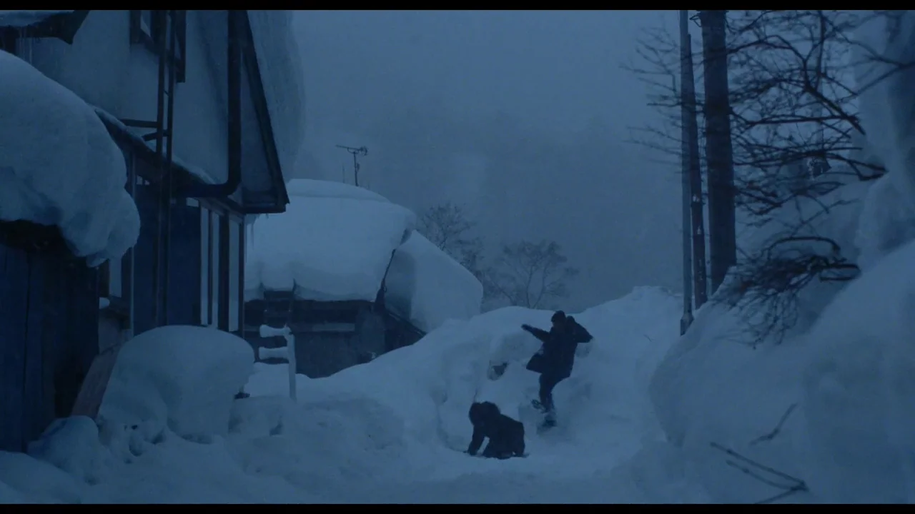 Millennium Mambo (2001) movie still: wide — A rural street in a winter climate is buried under massive drifts of snow. Two figures in dark clothing…