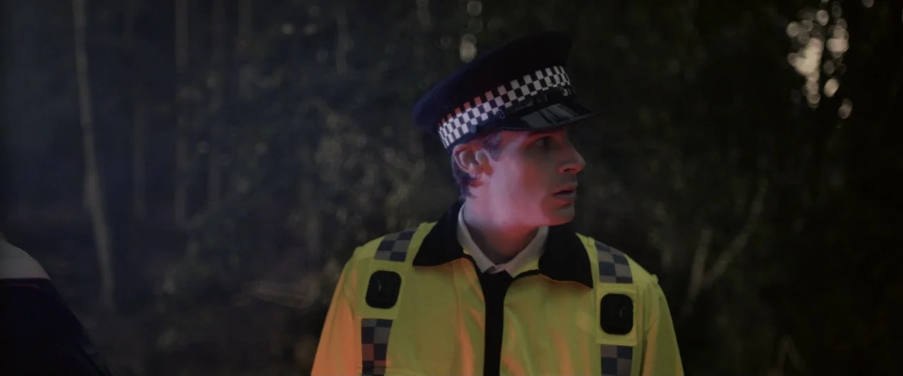 Winnie-the-Pooh: Blood and Honey 2 (2024) movie still: medium — A police officer stands in a dark, wooded area at night. The man looks to the side…