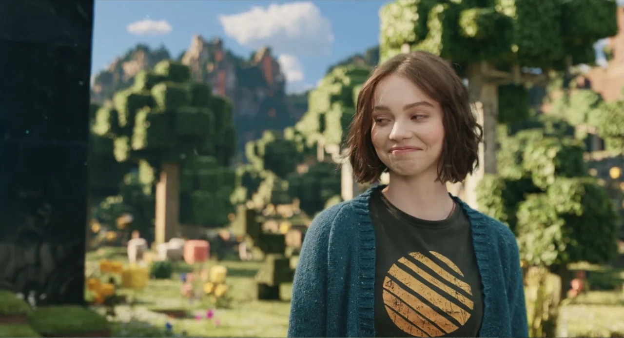 A Minecraft Movie (2025) movie still: medium — A woman stands in front of a blocky, voxel-based outdoor environment with square trees. She looks…