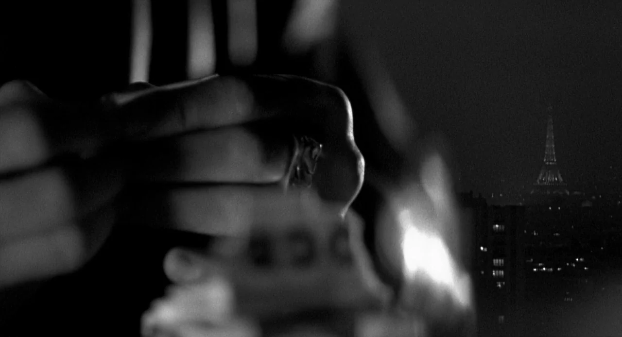 La Haine (1995) movie still: closeup — A dark rooftop overlooking a city skyline at night under low light conditions. The Eiffel Tower stands…