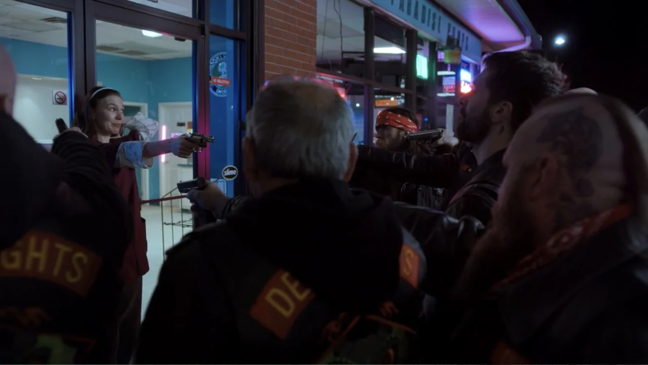 Burn (2019) movie still: medium — A group of men in motorcycle vests confront a woman through a glass door. The men point handguns at the woman…