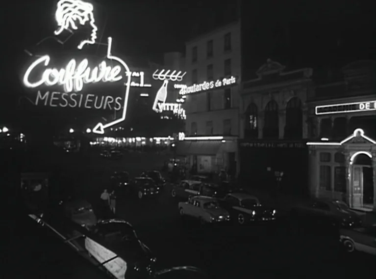 Head Against The Wall (1959) movie still: establishing — A nocturnal city intersection features illuminated neon storefront signs and several parked…