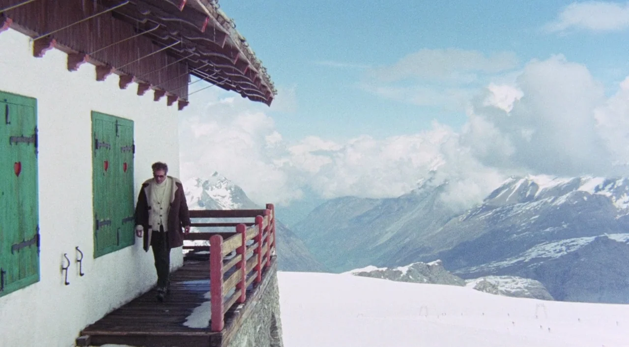The Iguana with the Tongue of Fire (1971) movie still: wide — A rustic mountain cabin with white walls and green shutters sits on a high ledge. A…