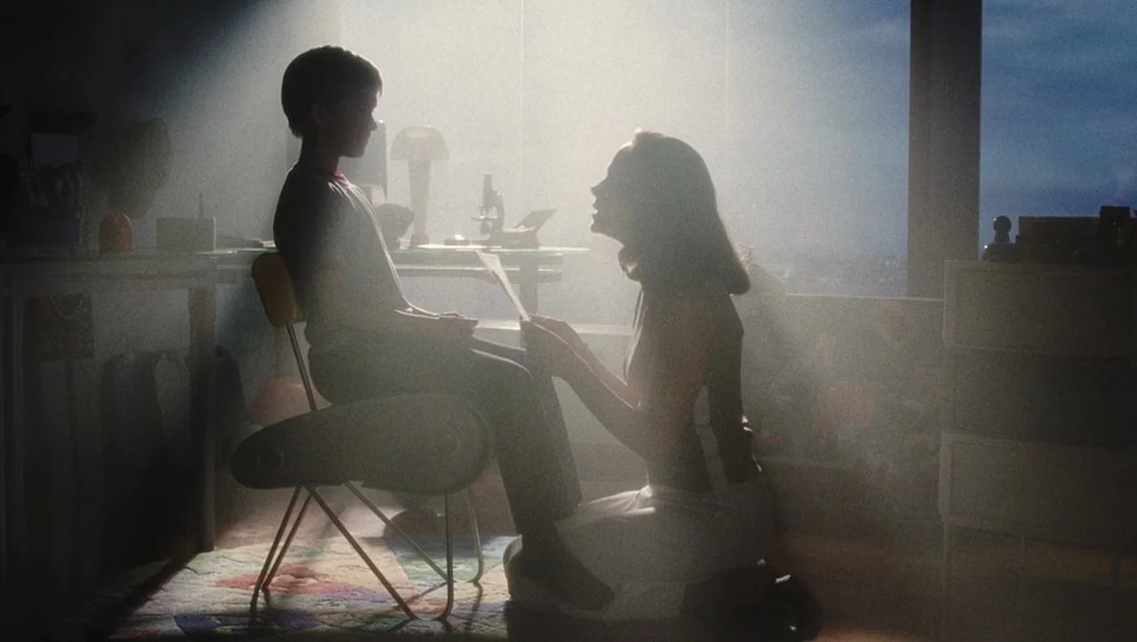 A.I. Artificial Intelligence (2001) movie still: medium — A sunlit room features a young boy seated in a chair facing a woman. The woman kneels on…