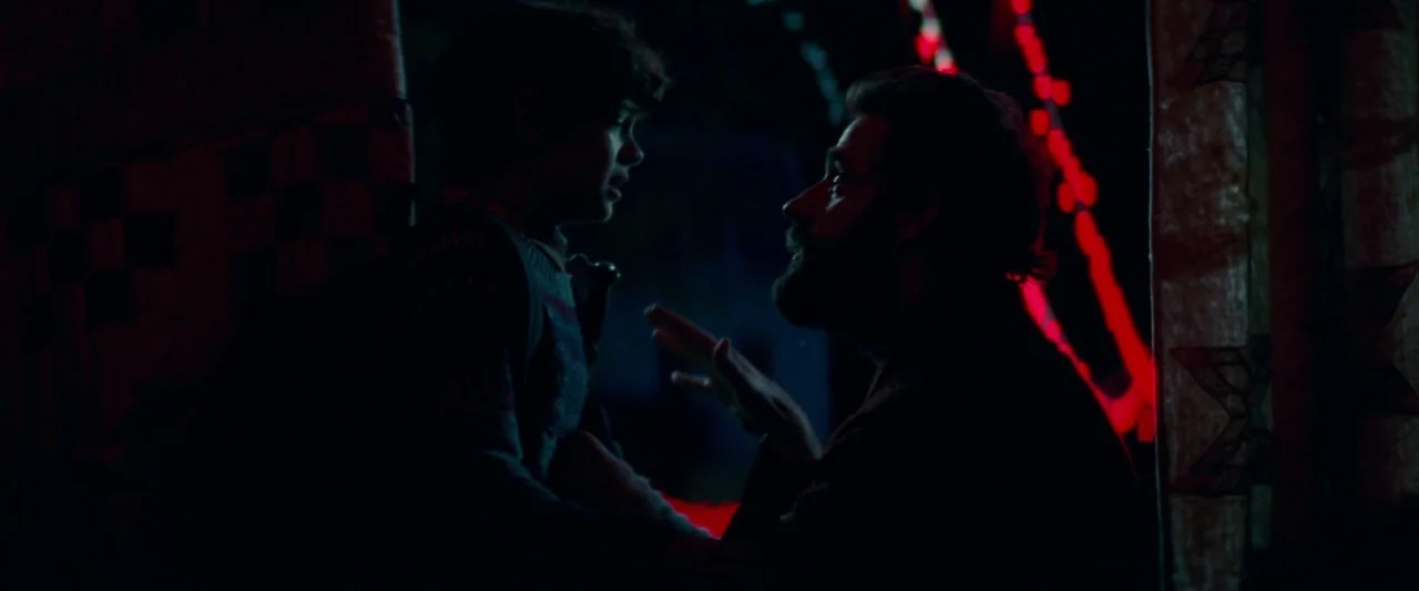 A Quiet Place (2018) movie still: medium — A dimly lit interior space features two figures interacting in low-key lighting. The man kneels before…
