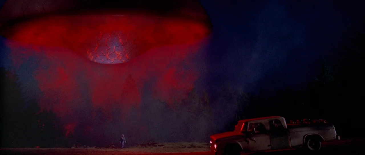 Fire In The Sky (1993) movie still: wide — A dark, rural landscape at night features a massive glowing red disc hovering above. A pickup truck sits…