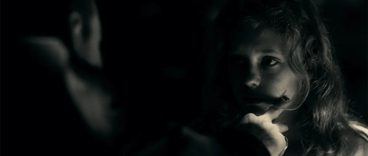 Blood Creek (2009) movie still: closeup — A dark indoor setting is almost entirely obscured by heavy shadows. A woman gazes towards an unseen figure…