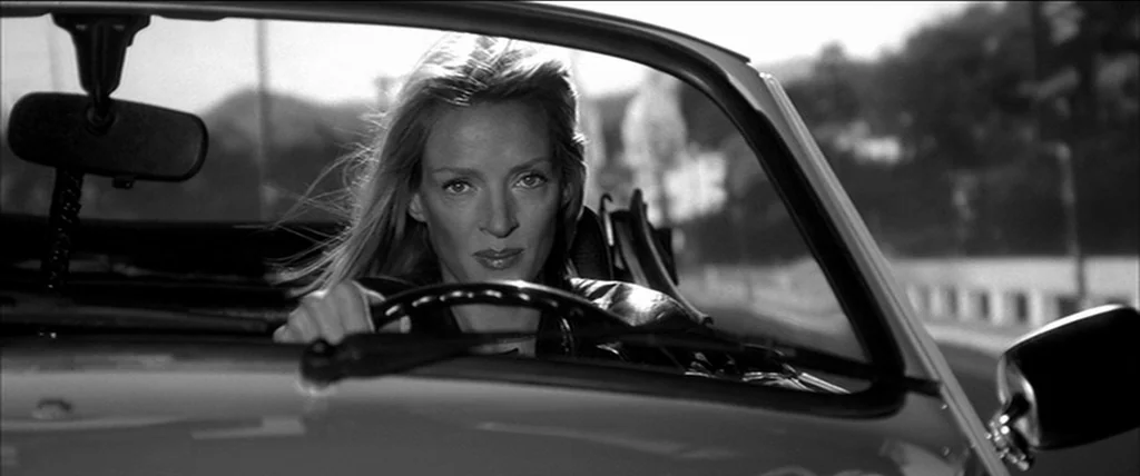 Kill Bill Vol. 2 (2004) movie still: medium — A blonde woman sits in the driver seat of a convertible car. She grips the steering wheel and looks…