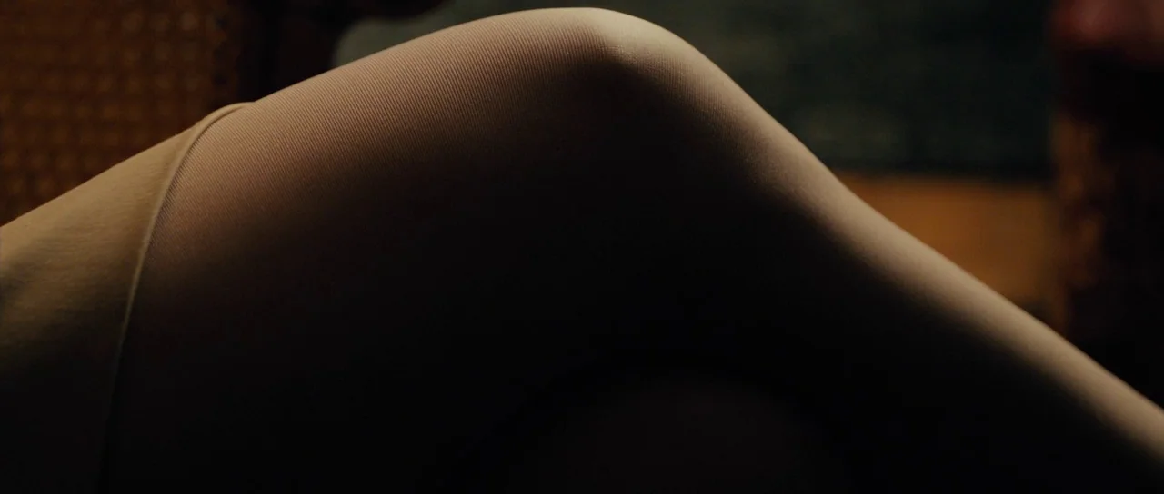 The Duke of Burgundy (2014) movie still: closeup — A close-up view shows the smooth, stocking-covered curve of a bent human knee. The background is…
