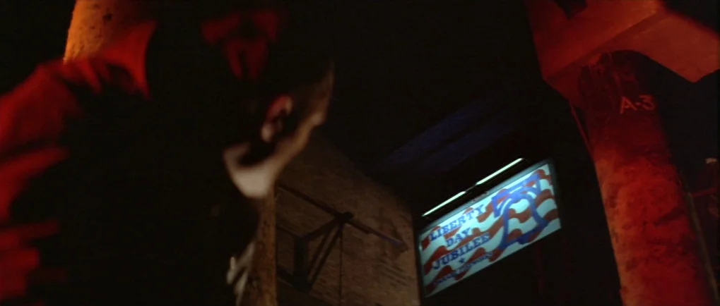 Blow Out (1981) movie still: closeup — A dark concrete parking structure features a pillar marked with an A-3 label. A glowing Liberty Day Jubilee…