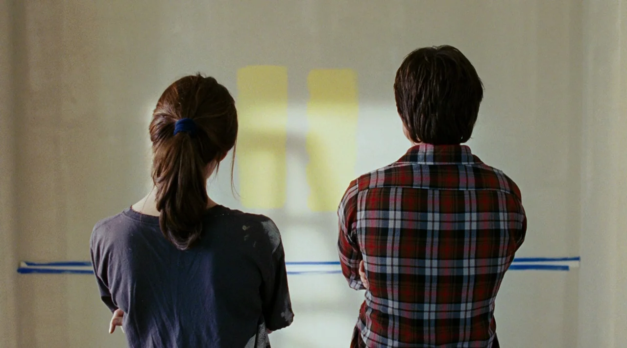 Juno (2007) movie still: medium — An unfinished room with beige walls features two distinct yellow paint test patches. A young man and woman stand…