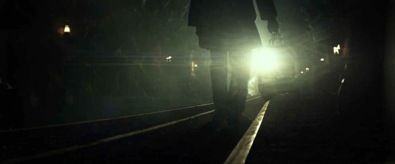 The Lone Ranger (2013) movie still: fullbody — A dimly lit narrow mine shaft has tracks running along the dirt floor. A solitary figure walks away…