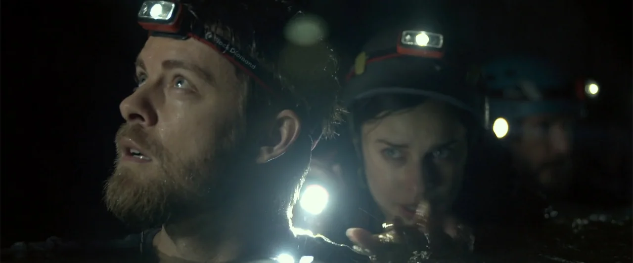 Black Water: Abyss (2020) movie still: medium — Three people swim through dark, murky water inside a damp subterranean cave environment. They wear…