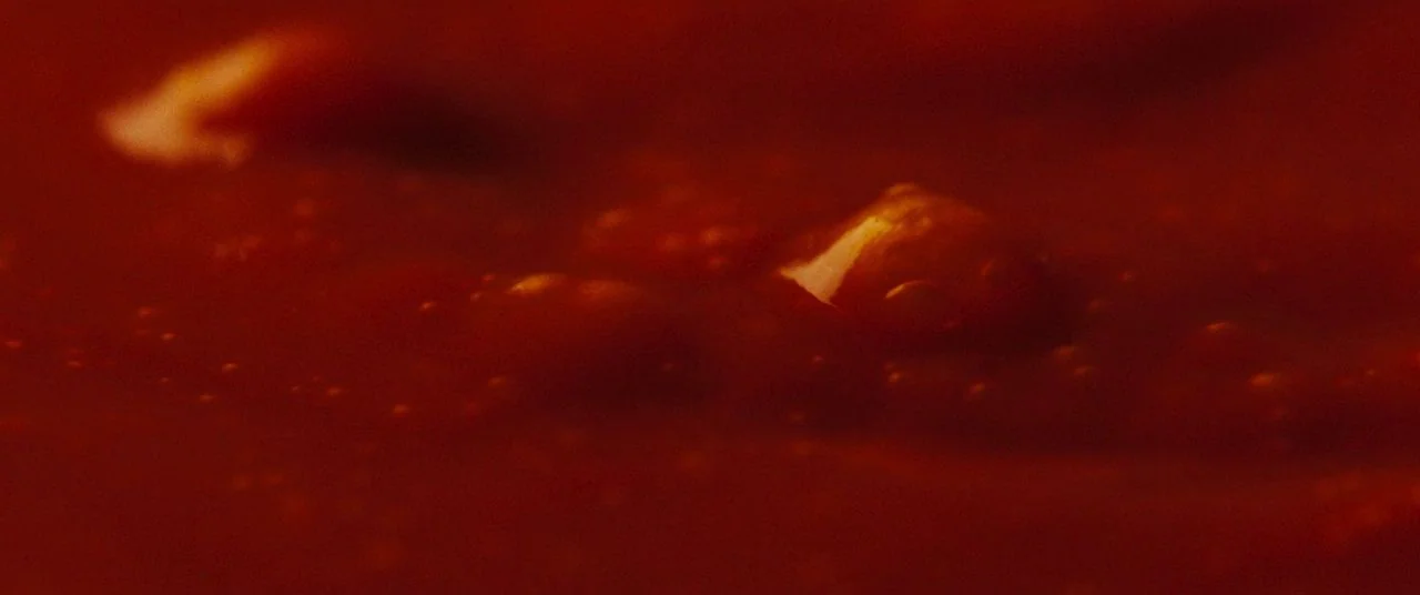 Saint Maud (2019) movie still: closeup — A close-up view of a thick red liquid simmering in a container. Small bubbles break the surface tension of…