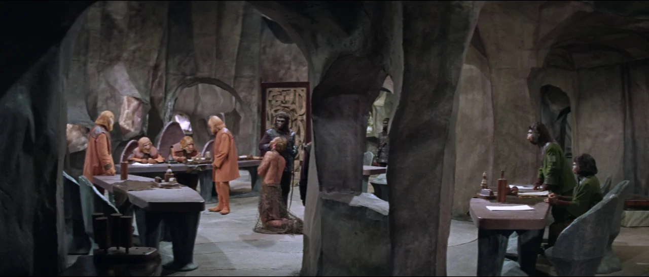 Planet of the Apes (1968) (1968) movie still: wide — A stone-walled interior with arched pillars and large carved tables arranged for council…