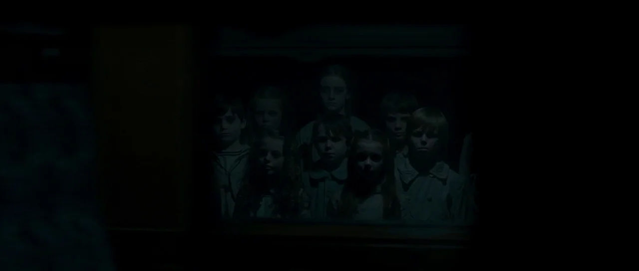 The Woman in Black (2012) movie still: medium — A dark, dimly lit corridor contains a group of children peering through a frame. The children are…