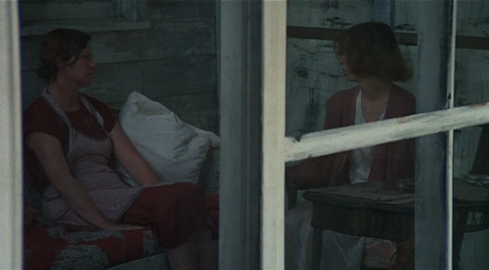 Thieves Like Us (1974) movie still: medium — A partially enclosed wooden porch area shows two distinct partitioned sections with textured walls. Two…