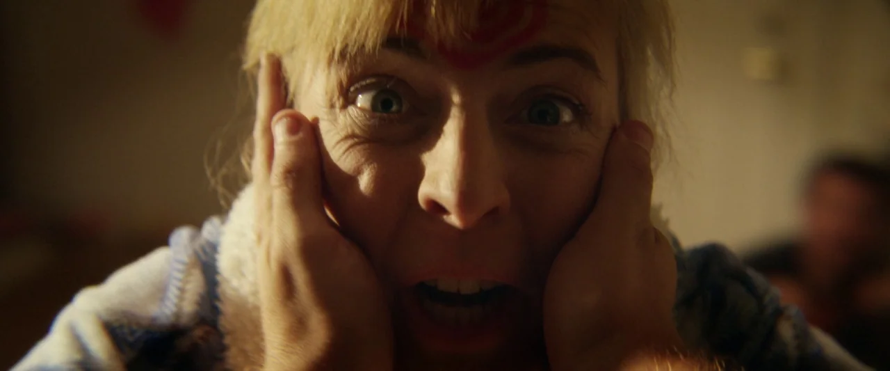 Seven Stages to Achieve Eternal Bliss (2018) movie still: closeup — A dimly lit room provides a dark background for the close-up shot. A blonde…