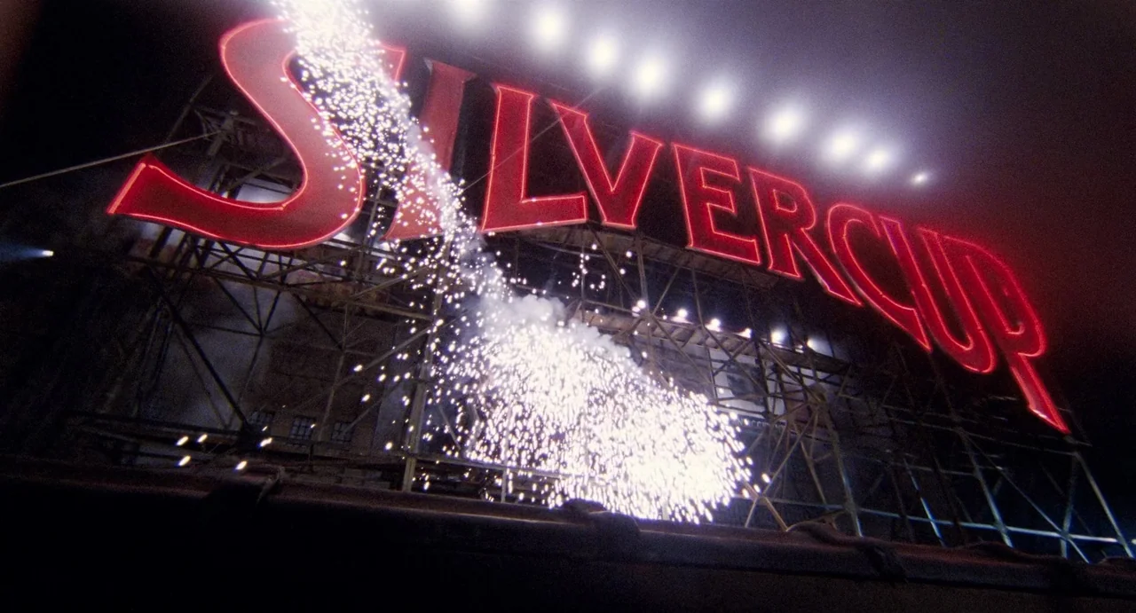 Highlander (1986) movie still: wide — A massive Silvercup neon sign is mounted on a complex industrial rooftop metal scaffolding. White sparks…