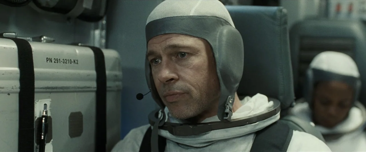 Ad Astra (2019) movie still: closeup — A compact, utilitarian spacecraft cockpit contains gray metal surfaces and industrial flight gear. A man…