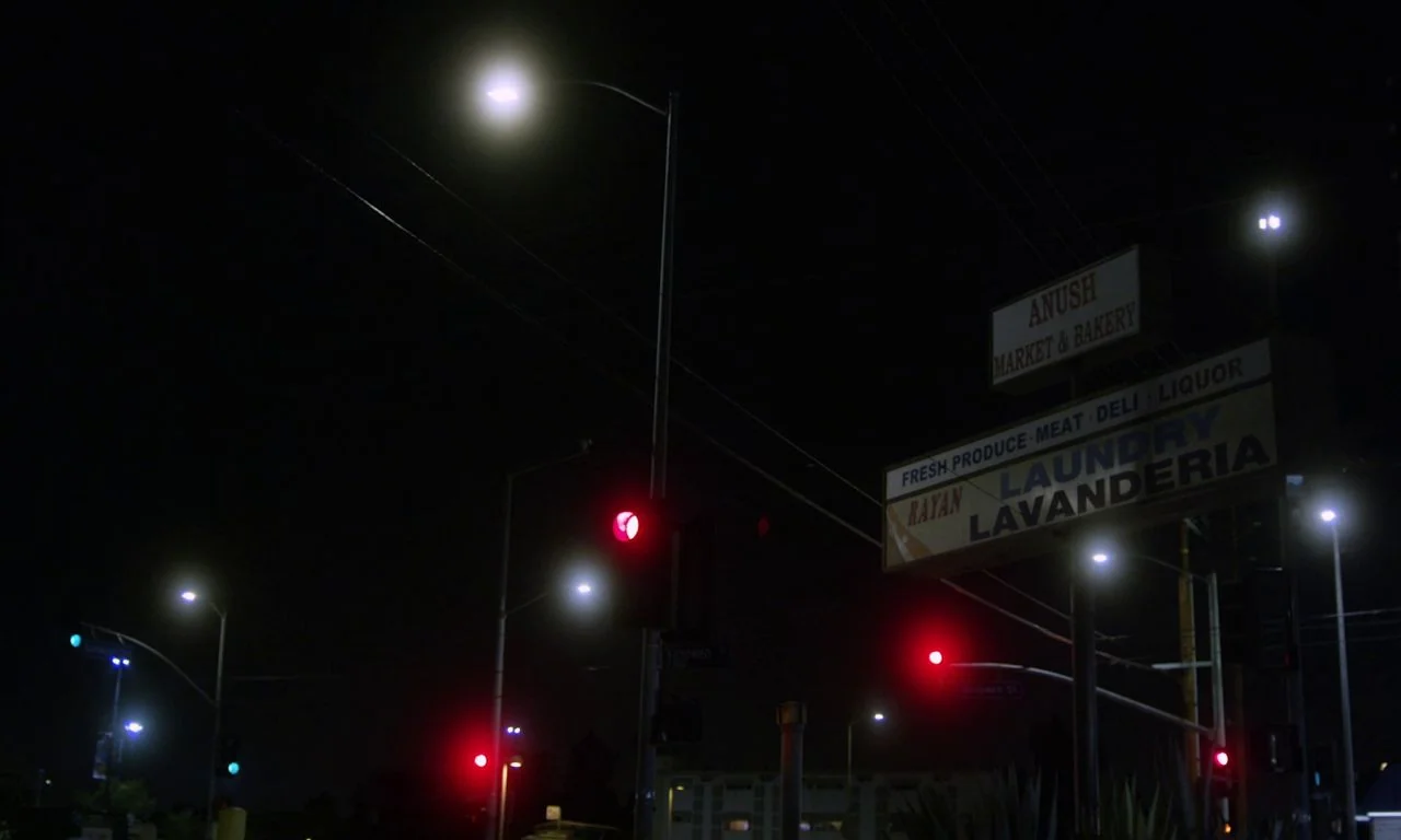 Ham on Rye (2019) movie still: establishing — A night view of a suburban street corner with illuminated business signs and signals. Streetlights…