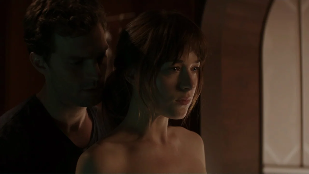 Fifty Shades of Grey (2015) movie still: medium — A dimly lit room with an arched doorway in the background. A man stands closely behind a woman…