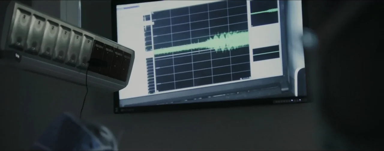 Hunting for Hedonia (2019) movie still: medium — A dimly lit hospital room features a mounted patient monitor displaying a cardiac waveform. The…