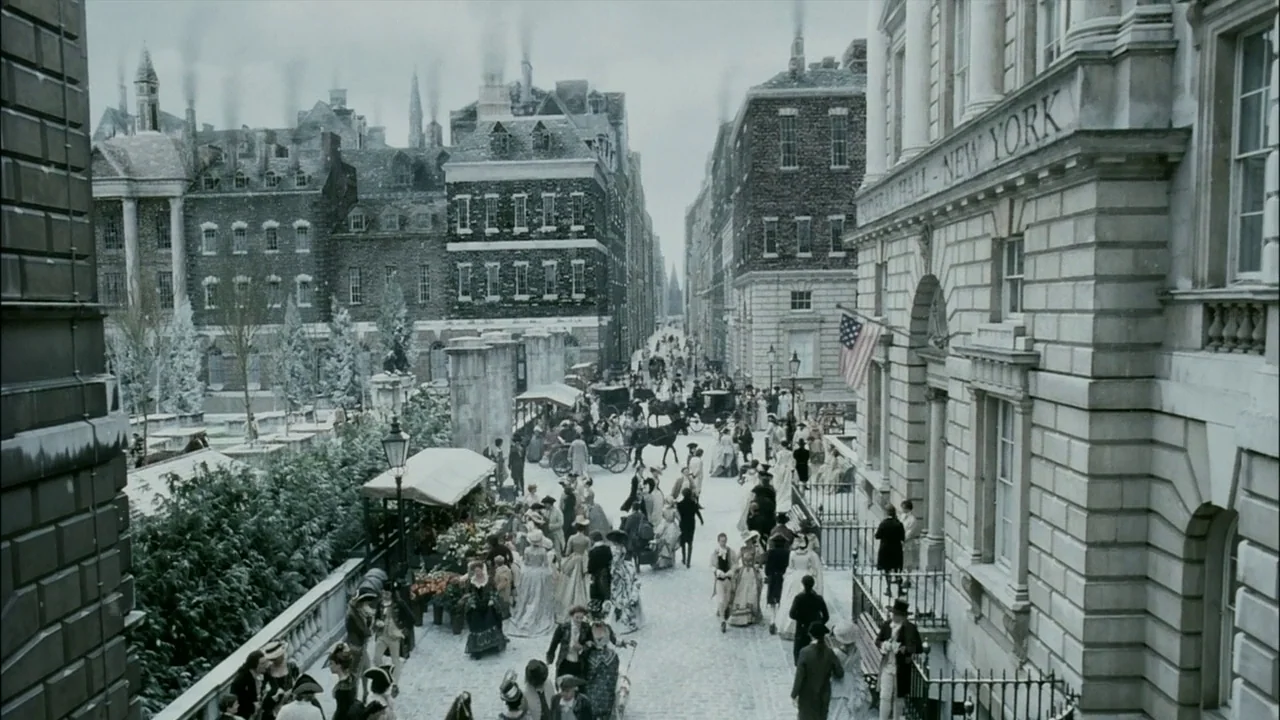 Sleepy Hollow (1999) movie still: establishing — A bustling 19th-century New York street scene shows stone buildings and horse-drawn carriages.…
