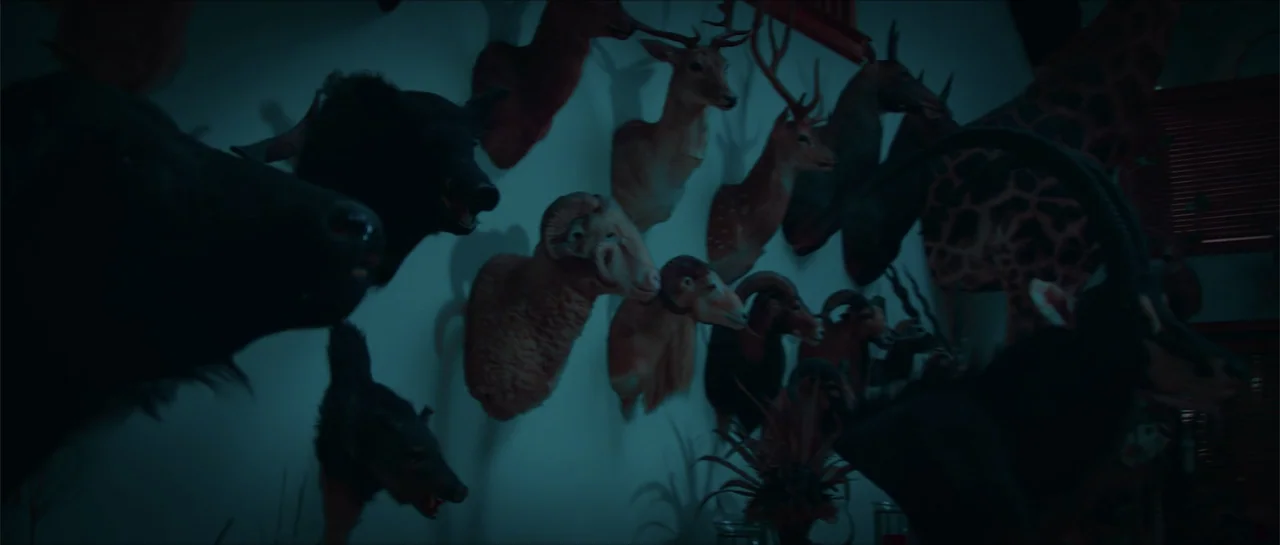 68 Kill (2017) movie still: medium — An interior wall is densely covered with numerous taxidermy animal heads including deer and rams. The room is…