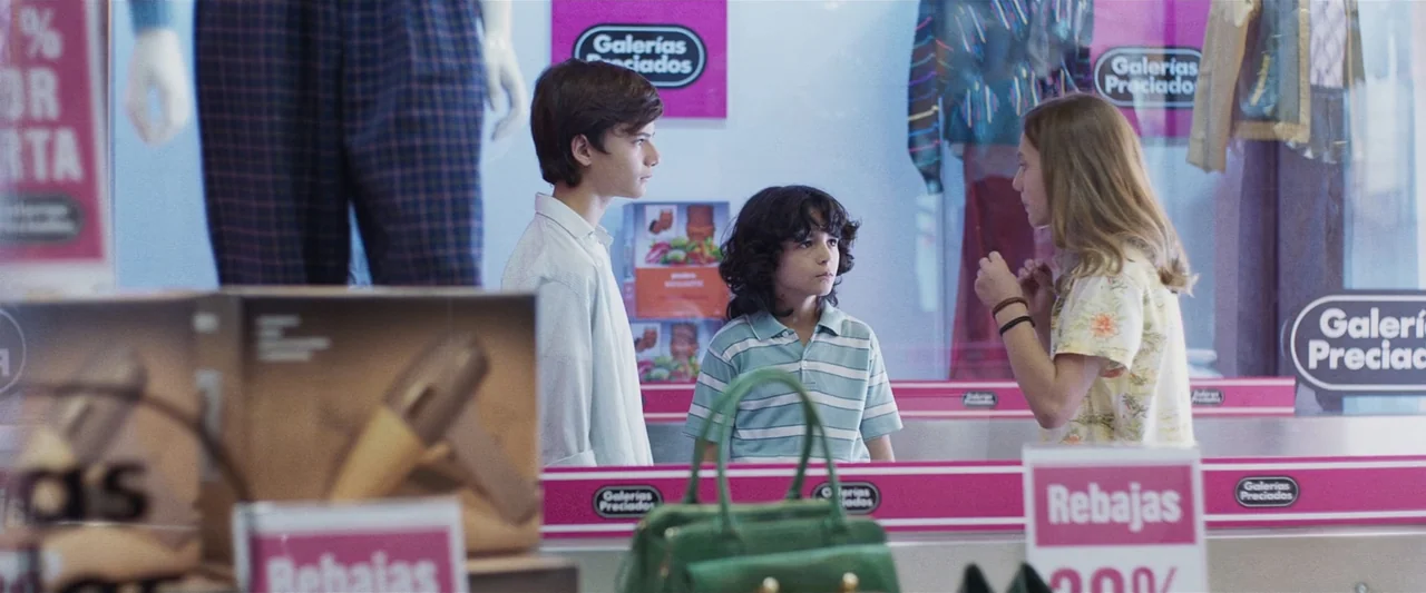 Voy a pasármelo bien (2022) movie still: medium — A glass display window at a retail store contains mannequins and various shopping products. Three…