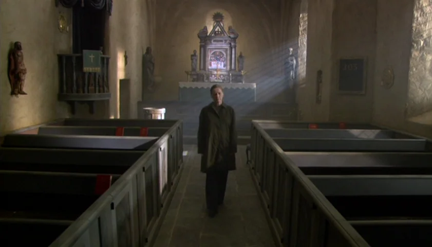 Saraband (2003) movie still: fullbody — The interior of an old stone church features rows of wooden pews and stone walls. An elderly woman walks…