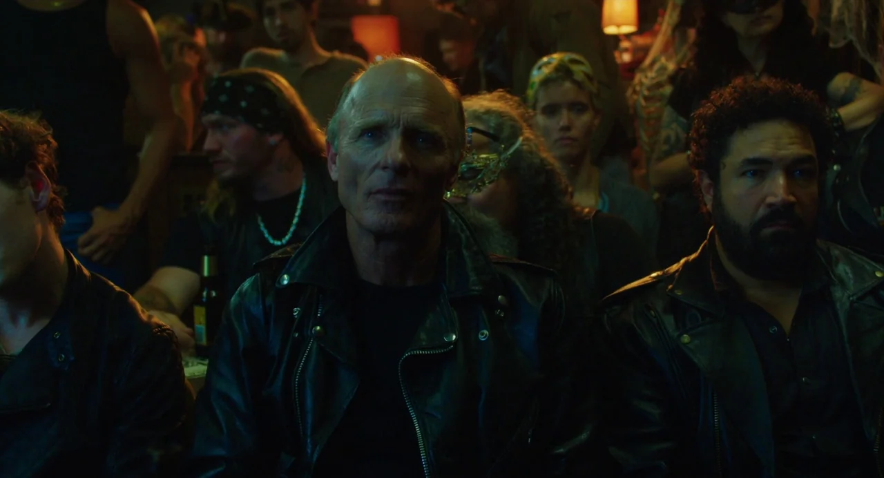 Cymbeline (2014) movie still: medium — A crowded dimly lit bar filled with people wearing leather and masks. A bald older man in a leather jacket…