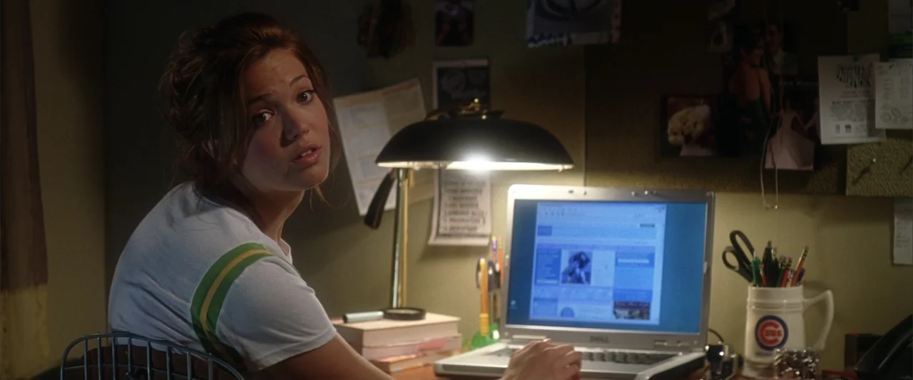 License to Wed (2007) movie still: medium — A dimly lit room contains a cluttered desk with a laptop and a pinboard. A young woman turns her head…