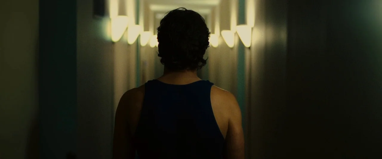Limitless (2011) movie still: medium — A dimly lit hotel corridor features rows of glowing sconces along the walls. A man in a dark tank top stands…
