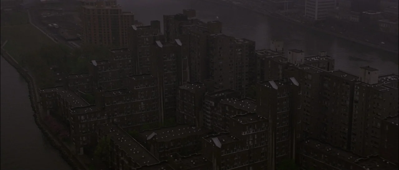 Dark Water (2005) movie still: establishing — A dense urban residential complex features multiple brown brick buildings situated alongside a river.…