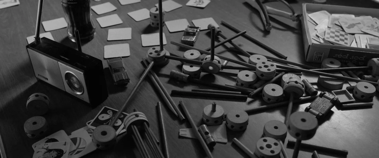 Roma (2018) movie still: wide — A cluttered wooden table surface is covered in scattered construction toy parts and cards. A vintage radio and small…