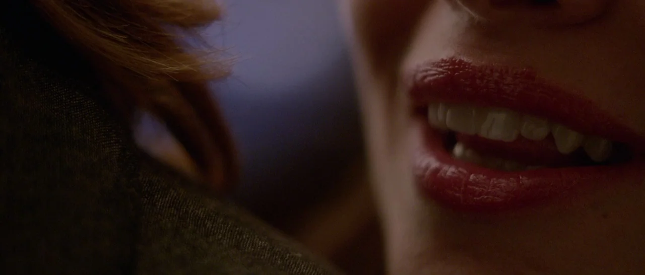 The Invitation (2015) movie still: closeup — An extreme closeup focuses on a person's mouth with part of their hair visible. The lips are slightly…
