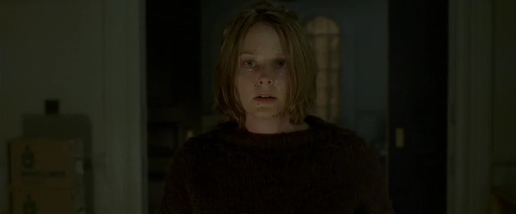 Panic Room (2002) movie still: medium — A dark, dimly lit domestic hallway with plain walls and a distant arched doorway. A young woman with short…