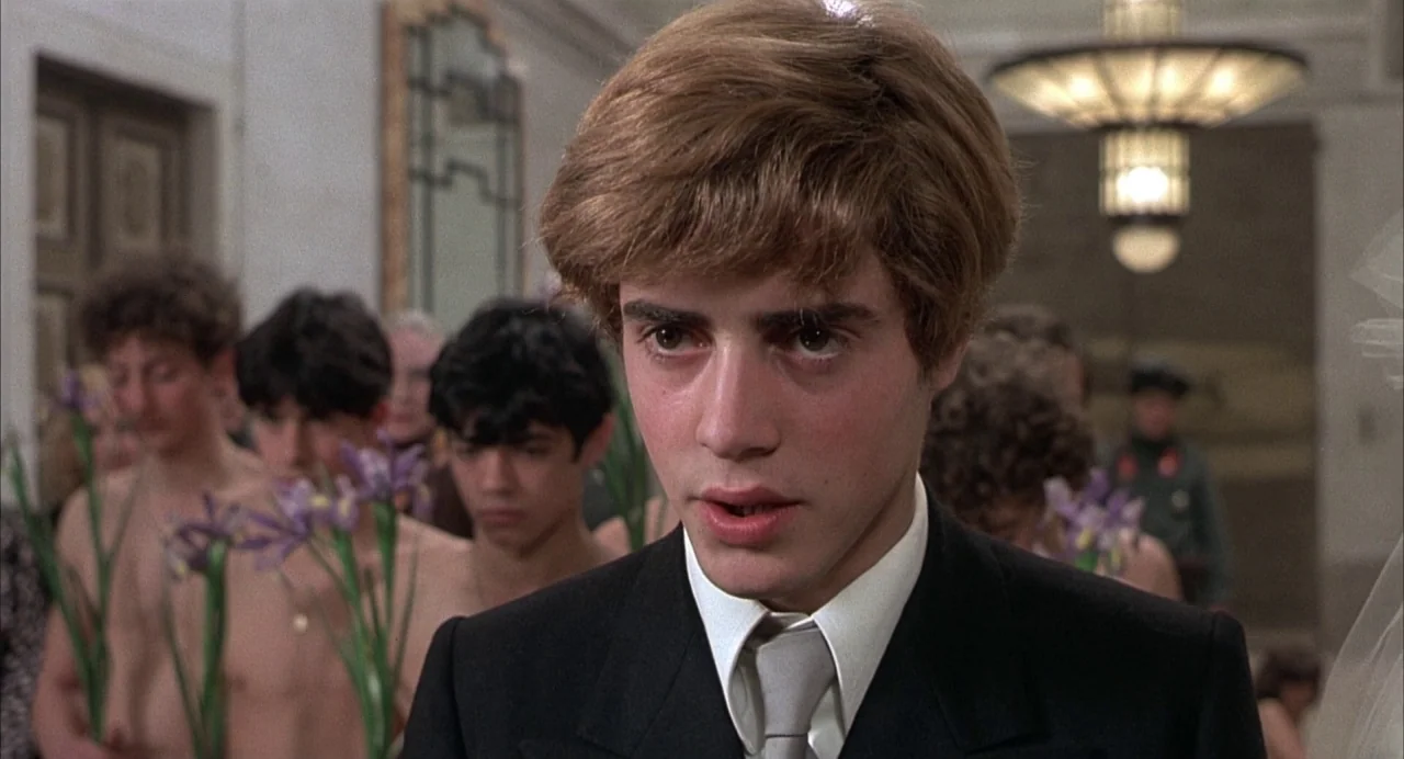 Salò, or the 120 Days of Sodom (1975) movie still: closeup — A formal interior space features an ornate chandelier and reflective wall panels. A…