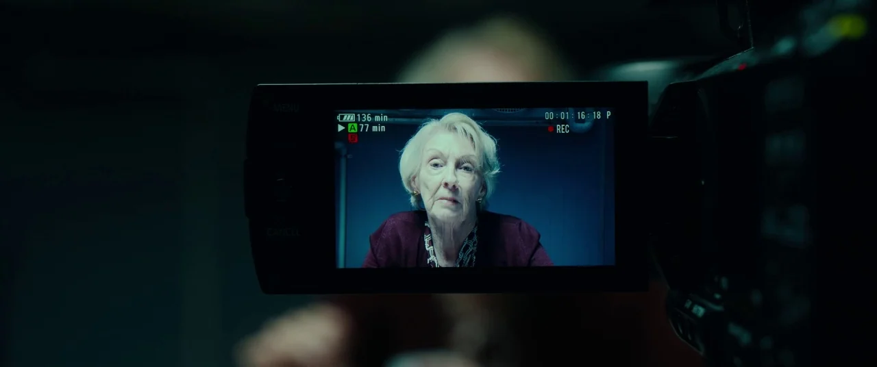 Okja (2017) movie still: closeup — An older woman is framed within the display screen of a professional digital video camera. The background is a…