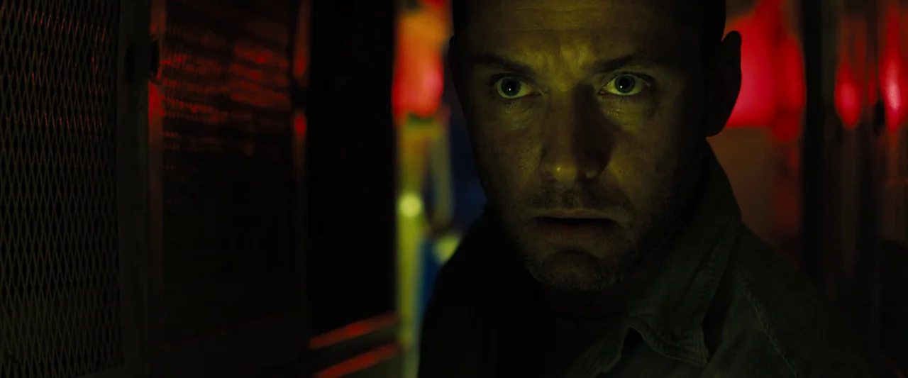 Black Sea (2014) movie still: closeup — A dark narrow passageway is lit by sharp red neon signs and yellow light. A man in his forties with short…