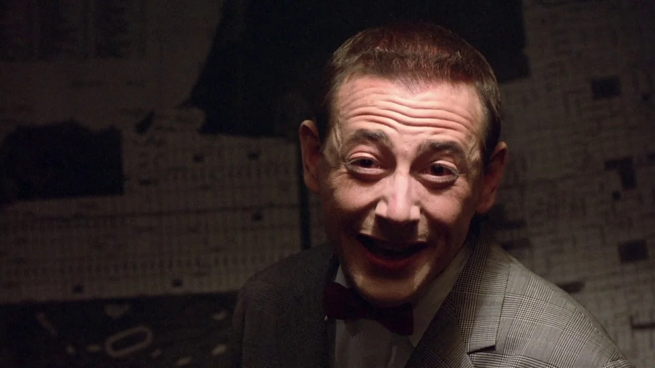 Pee-Wee’s Big Adventure (1985) movie still: closeup — A man stands in a dark room with blurred, indistinct patterns on the wall. He looks directly…