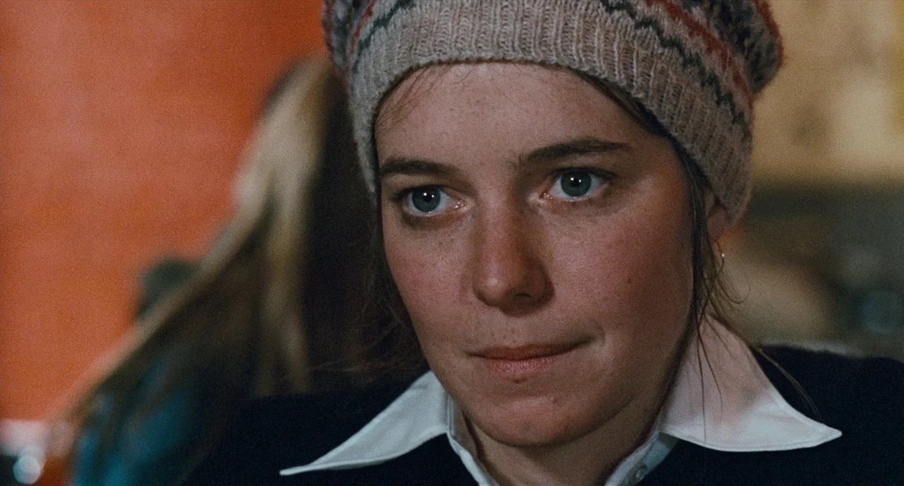The Panic in Needle Park (1971) movie still: closeup — A woman wears a patterned beanie inside a dimly lit space with warm walls. She looks ahead…