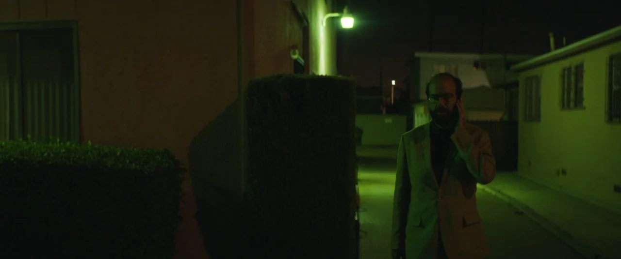 Lemon (2017) movie still: medium — A narrow alleyway at night illuminated by a single flickering fluorescent light. A man in a suit walks towards…