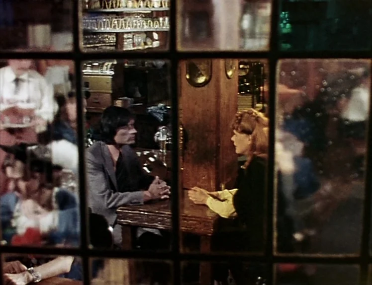 Martha (1974) movie still: medium — A dimly lit pub with dark wooden furniture seen through a leaded glass window. A man and a woman sit at a small…